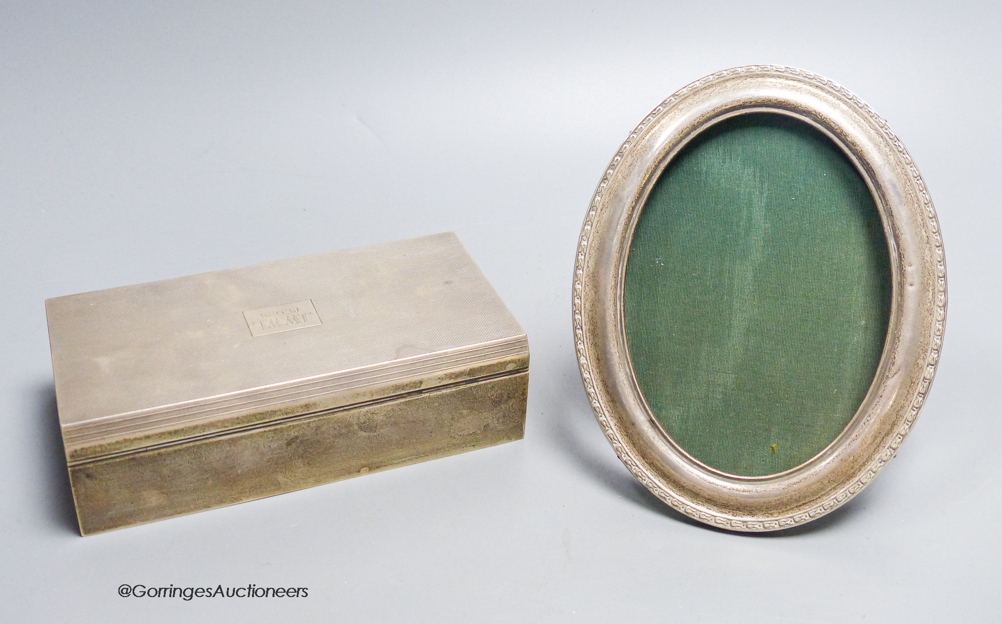 A 1940's engine turned rectangular silver mounted cigarette box, with engraved inscription, 17cm and a silver mounted oval photograph frame.